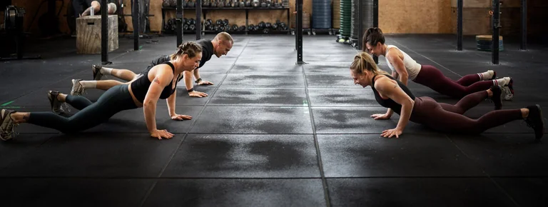 Four people performing push-ups on a gym floor